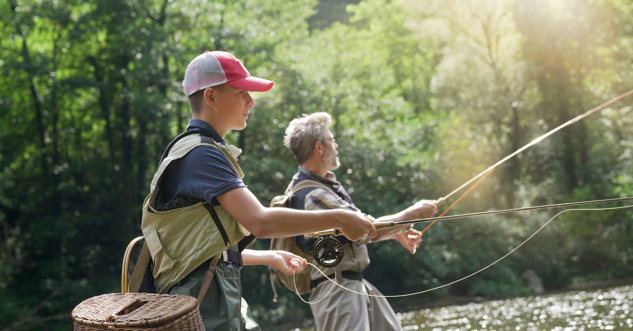 A father and his son fly fishing in summer on a beautiful trout river with clear water